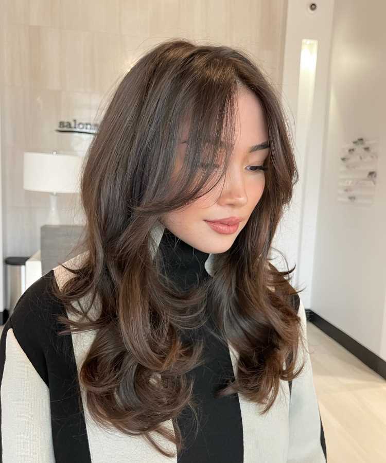 A imagem mostra uma pessoa com um corte de cabelo longo e repicado, em camadas. As camadas criam movimento e volume, enquanto a franja é longa e levemente desfiada, emoldurando o rosto de forma suave. Esse estilo é frequentemente chamado de "corte em camadas repicadas" ou "corte em camadas longas", popular por sua versatilidade e por adicionar textura ao cabelo.


