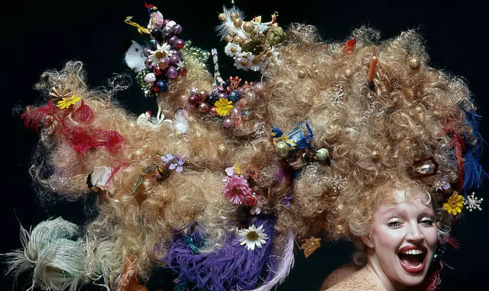 Foto colorida de Elke Maravilha jovem posando sorrindo com um sorriso aberto, com o cabelo loiro muito longo e armado, enfeitado com inúmeros objetos. Elke Maravilha posando sorrindo com um sorriso aberto, com o cabelo loiro muito longo e armado, enfeitado com inúmeros objetos.