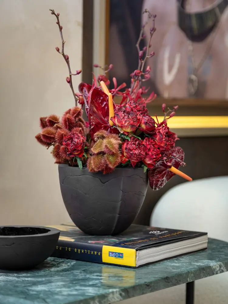 Mesa verde com tigela preta, livro e vaso com planta rosa