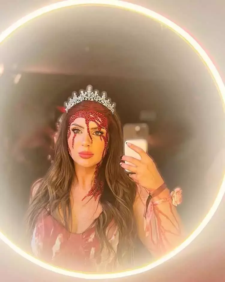 Mulher de pele clara usando maquigem halloween sangue falso com brilhos vermelhos, coroa e vestido com sangue