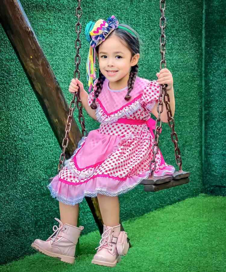 Menina sentada em balanço usando vestido rosa de festa junina