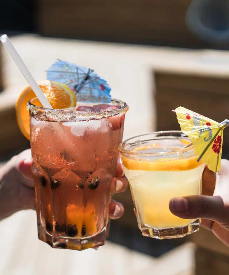 Mãos segurando drinks decorados com guarda-chuva.