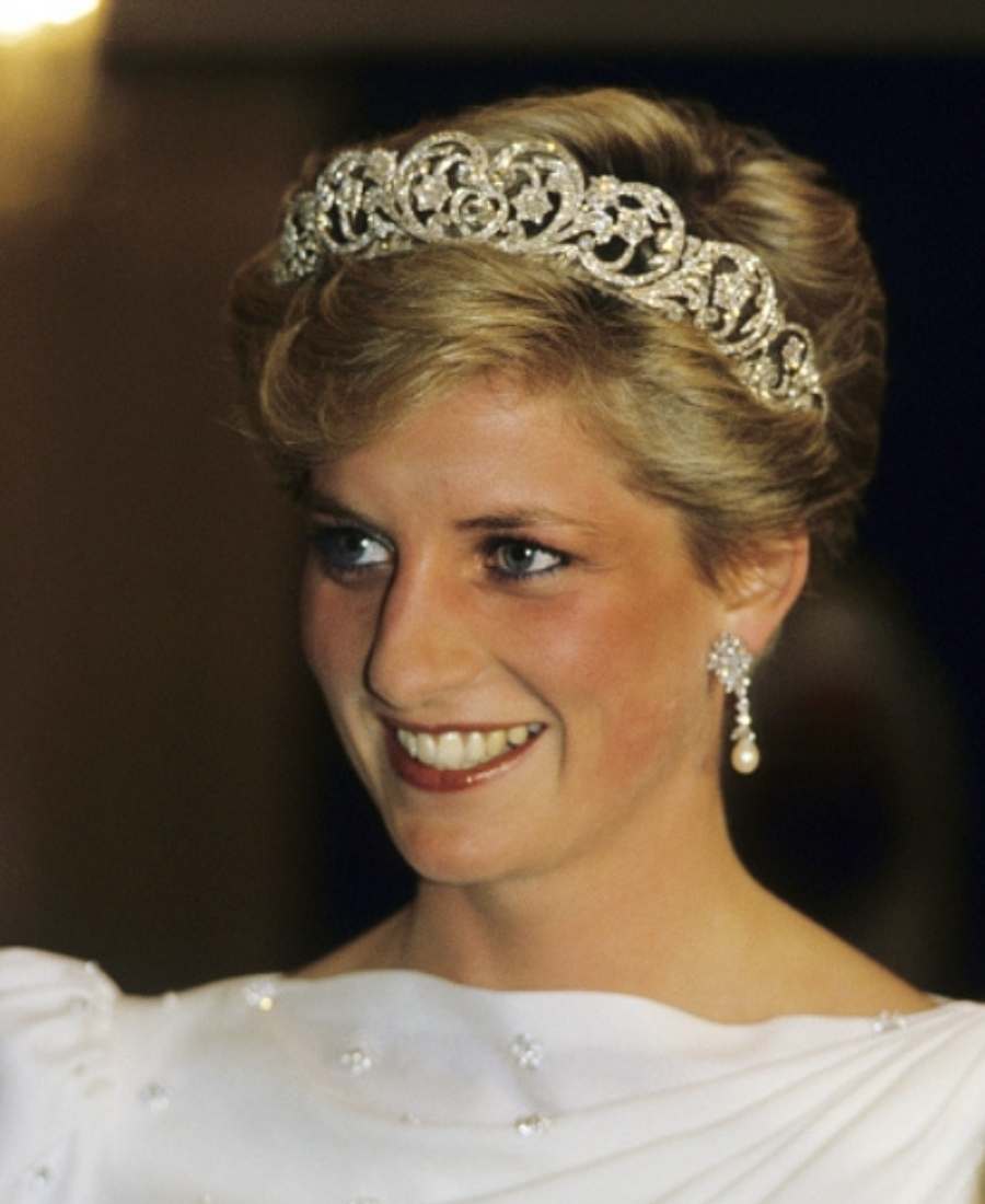 Foto  da princesa de Gales sorridente. Ela está de frente e usa Tiara Spencer, brincos e roupa branca com pedras.