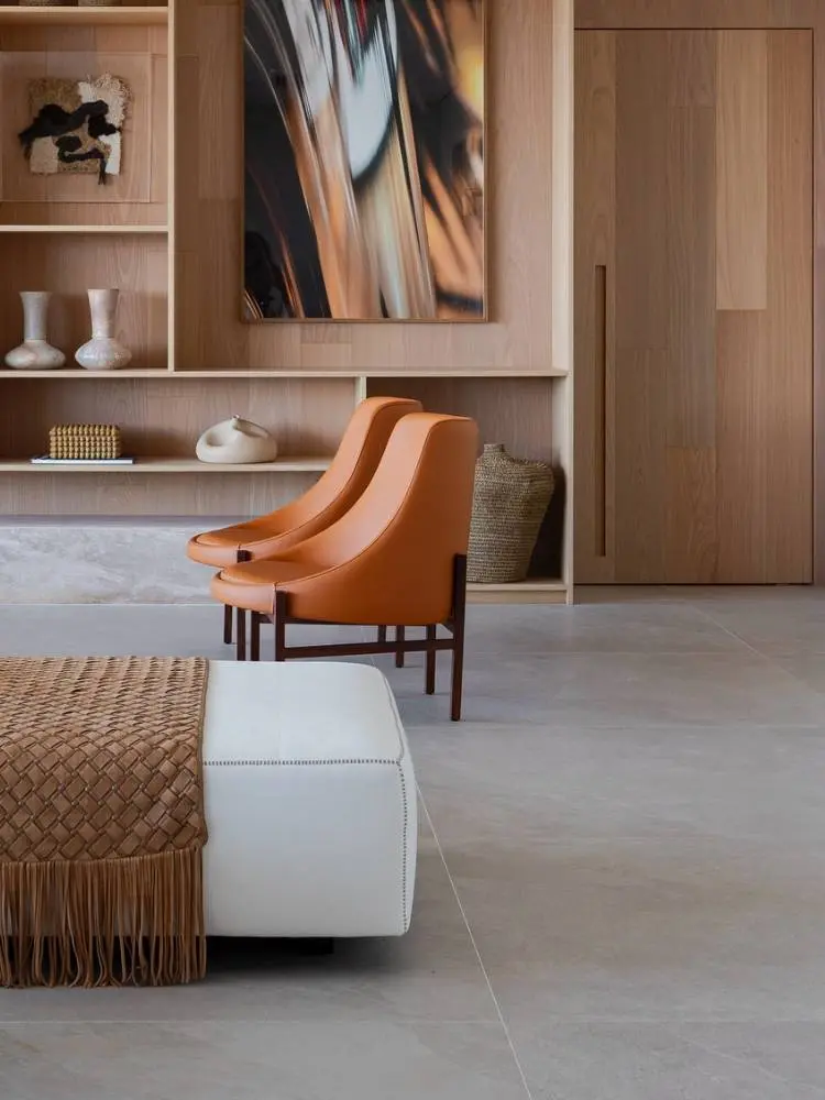 Duas poltronas laranjas em couro, em sala com sofá branco e estante de madeira