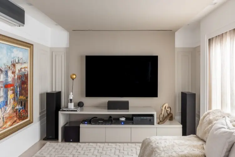 Sala de TV com aparador, sofá bege, quadro colorido, parede com moldura 