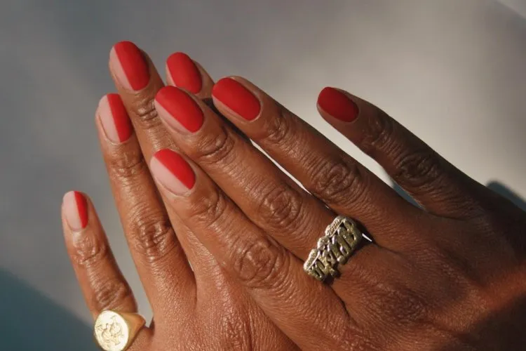 Mãos de pessoa de pele negra com unha redonda curta, metade transparente e metade vermelha 