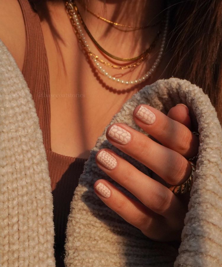 A imagem mostra uma mão com unhas bem cuidadas, decoradas com uma fina linha metálica na ponta, em um estilo conhecido como "francesinha invertida" ou "unhas francesas modernas". A pessoa está usando vários anéis dourados, alguns com pedras grandes e outros com detalhes de pérolas. O pulso tem uma pulseira brilhante. A luz na imagem destaca o brilho dos acessórios e o esmalte das unhas.
