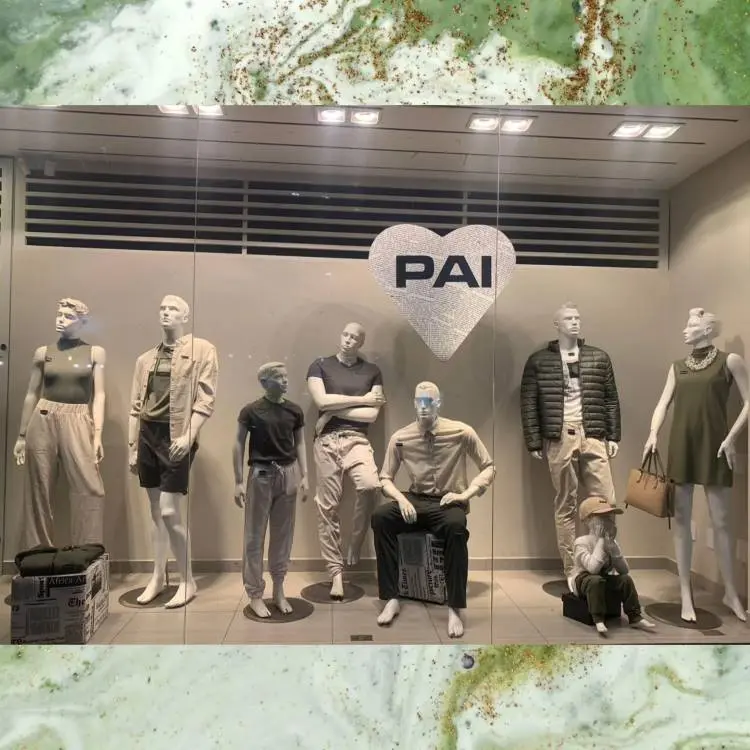 A imagem mostra uma vitrine de loja com múltiplos manequins de adultos e crianças exibindo diversas peças de roupa. Ao centro, um grande coração com a palavra "PAI" decora o vidro, indicando uma celebração do Dia dos Pais.