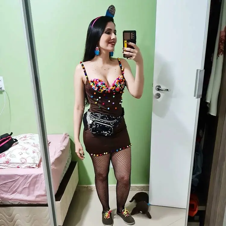 Foto de mulher fantasiada de cupcake com tiara, vestido marrom com pompons coloridos