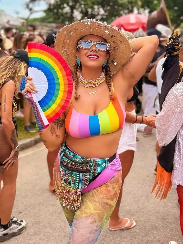 Mulher de pele clara usando chapéu, top colorido, leque colorido, hot pant rosa e bolsa de miçangas