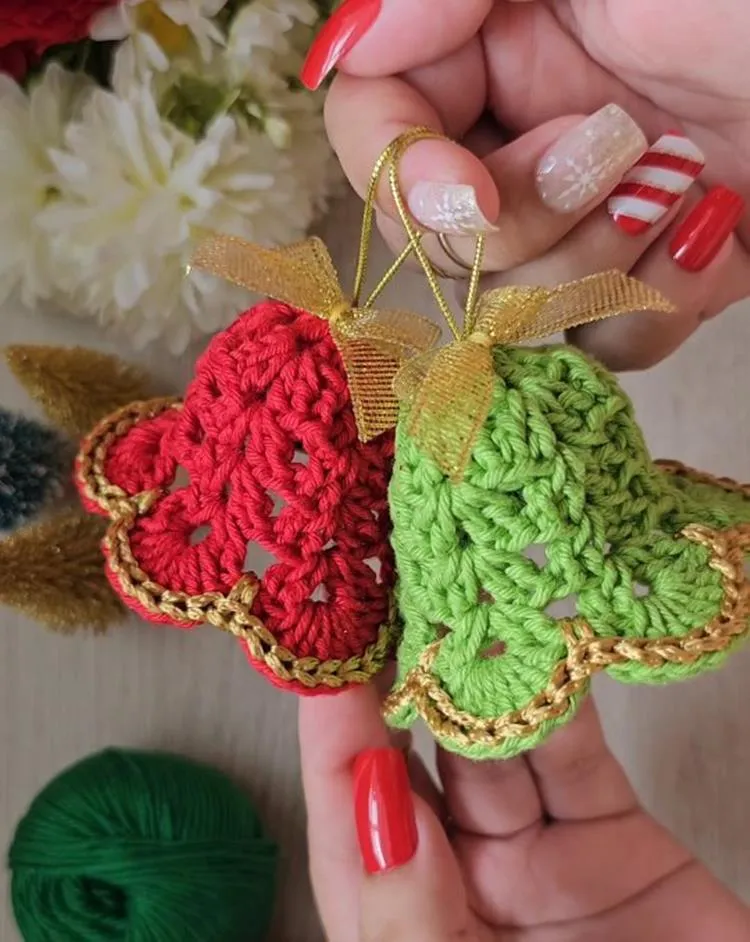 Mãos com unhas natalinas segurando Sinos de Natal de crochê vermelho e verde com detalhes dourados