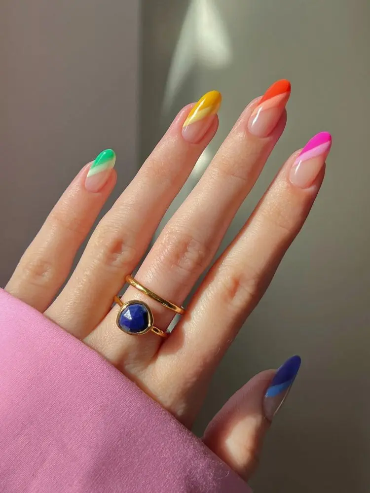 Mão de pele clara com unhas almon nudes com francesinhas diagonais em cores do arco-íris