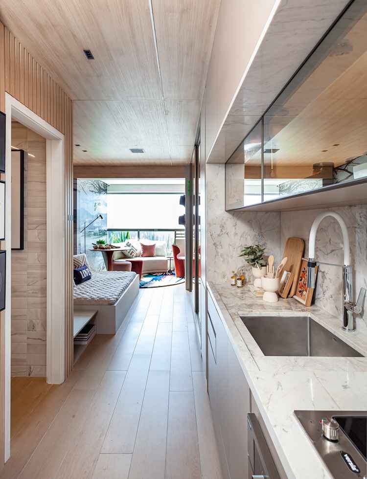 foto de apartamento com todos os espaços integrados, sala/quarto, cozinha e varanda, com chão de madeira, pia de mármore e decoração em tons terrosos