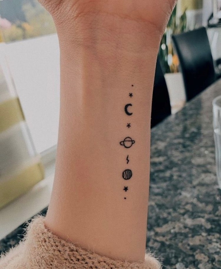 Tatuagem no pulso com estrelas, lua e planetas