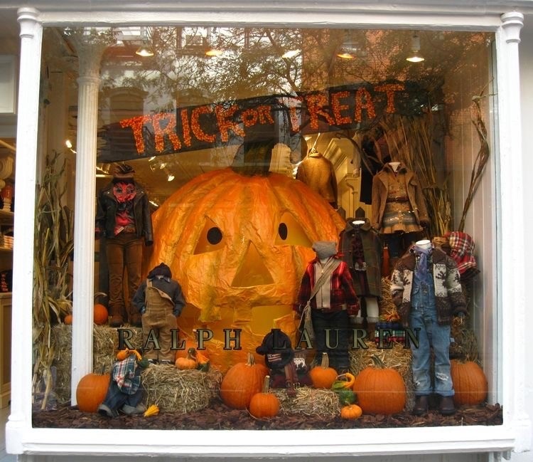 Vitrine infantil com decoração de Halloween, com abóboras de diferentes tamanhos, roupas e faixa escrito "trick or treat"
