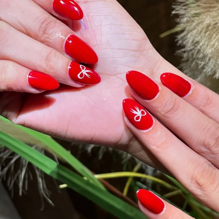 Unhas almond vermelhas com laço branco no anelar 
