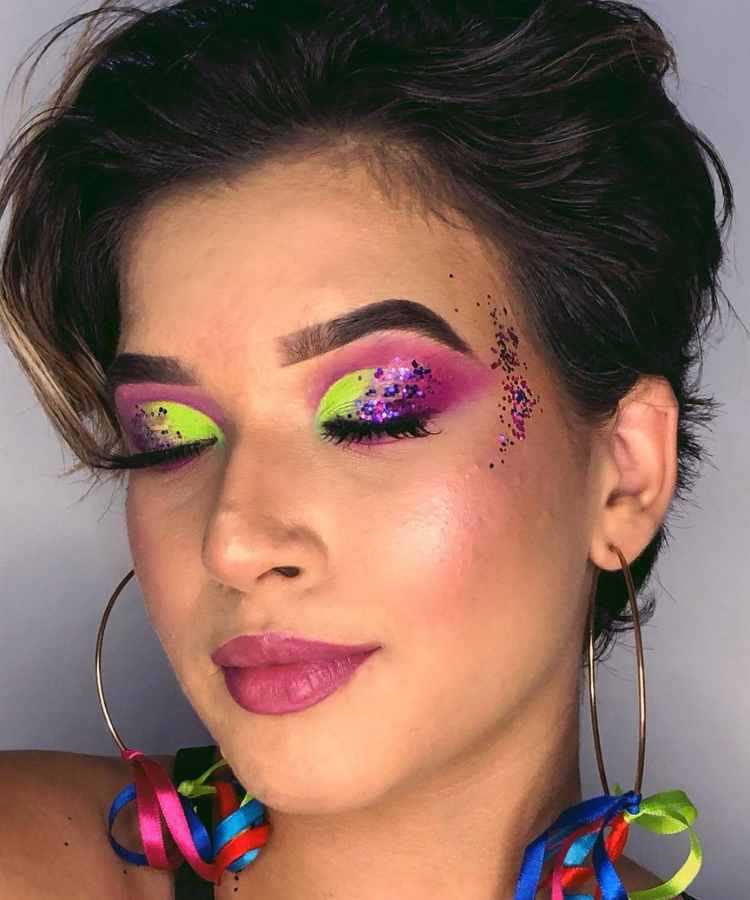 Mulher de pele clara usando sombra roxa e verde, glitter e batom rosa 