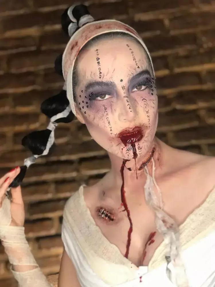 Mulher de pele clara fantasiada de múmia, com bandagens ensanguentadas, sangue falso na boca, rosto pálido, desenho de veias e olhos roxos