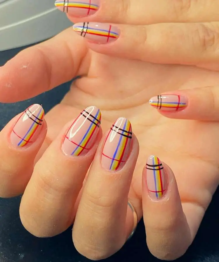 
Unhas ovais com esmalte nude translúcido e padrão xadrez delicado. As listras finas em vermelho, amarelo e azul, com duas mais grossas em preto na ponta de cada unha, criam um design moderno e elegante.
