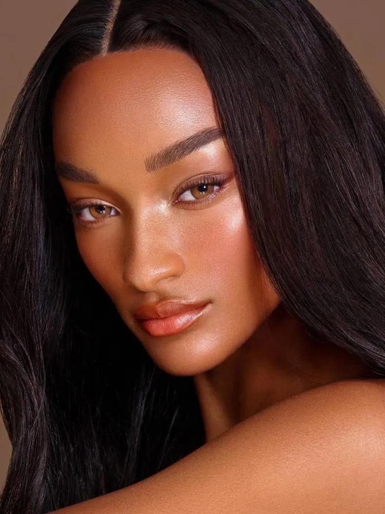 Mulher de pele negra usando make neutra e leve, com poucos produtos. 