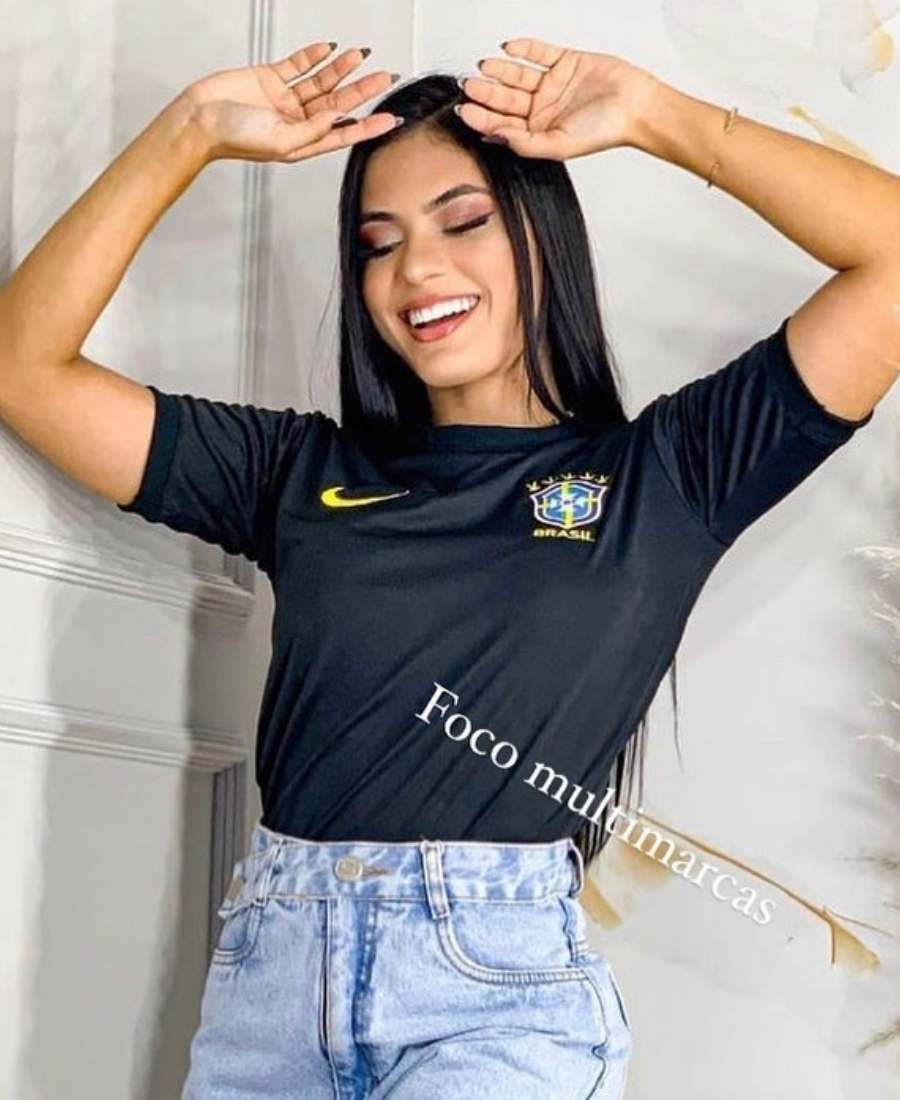 Imagem com fundo parede branca. No centro, mulher usando roupas para a copa do mundo: camiseta preta do Brasil + short jeans.