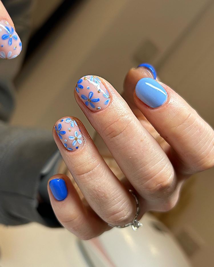 Unha rosada e azul de Dois Tons: um Claro e um médio. as unhas rosadas possuem flores azuis e brancas mescladas com bolinhas e dourado