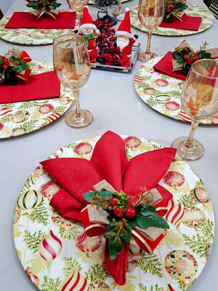 Mesa posta com sousplat de tecido de bolas natalinas, com arranjo no guardanapo. 