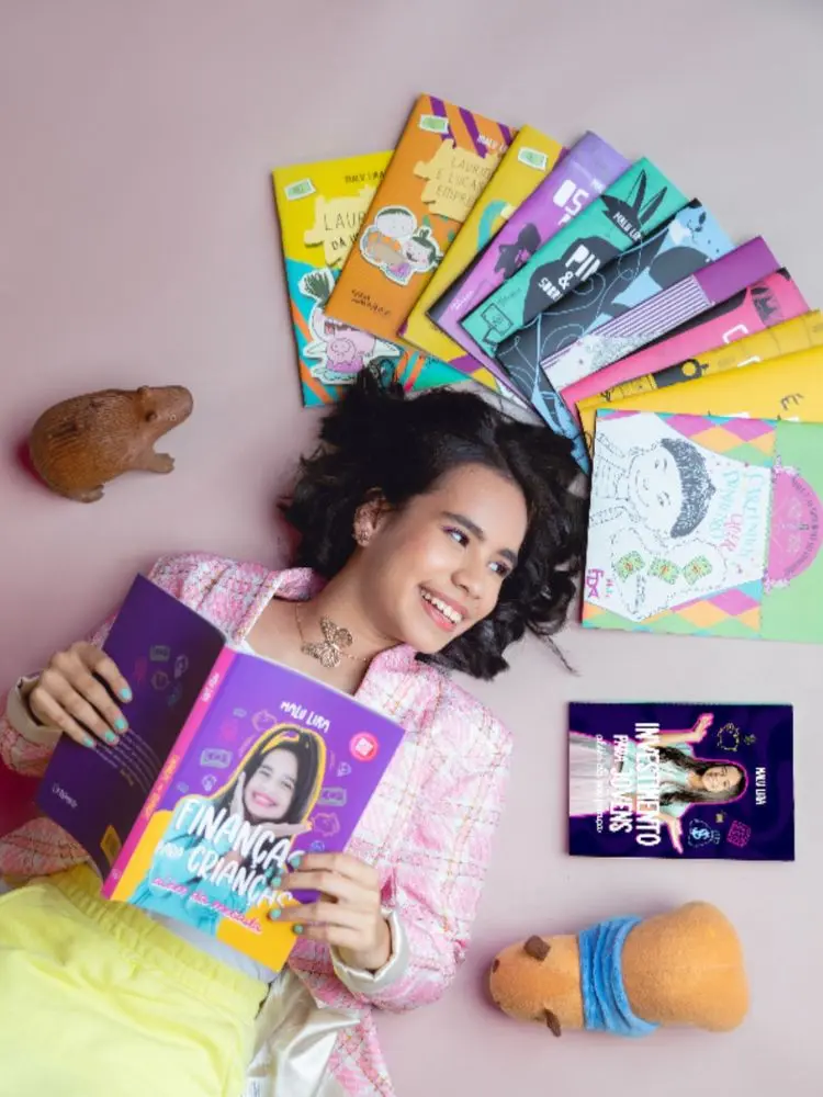 Malu Lira deitada segurando um livro e com vários próximos à cabeça 