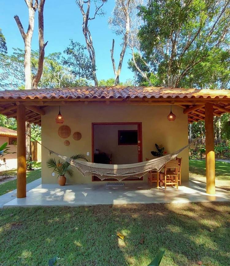 entrada de lar amarela, com rede na varanda, ao redor de árvores e gramado