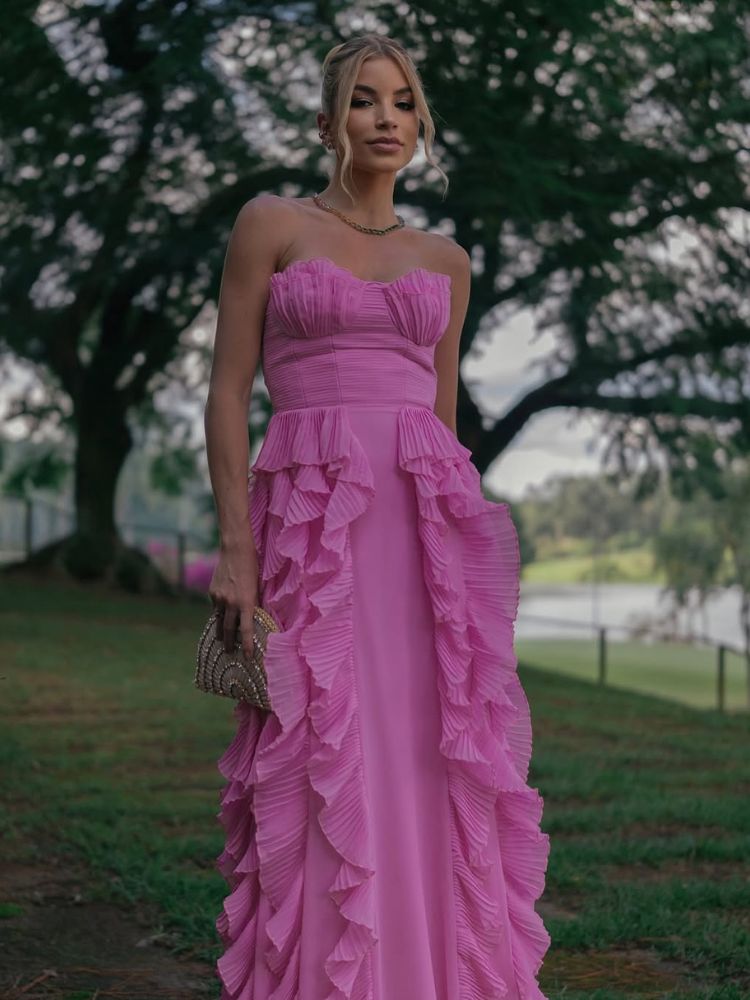 Mulher de pele clara usando vestido rosa com detalhes nos seios e babados 