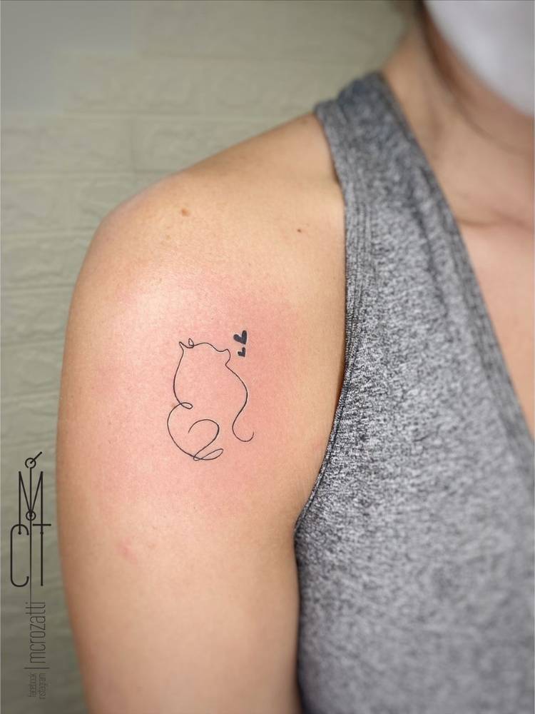 Mulher de pele clara e regata cinza com tatuagem no ombro de contorno fine line de cachorro