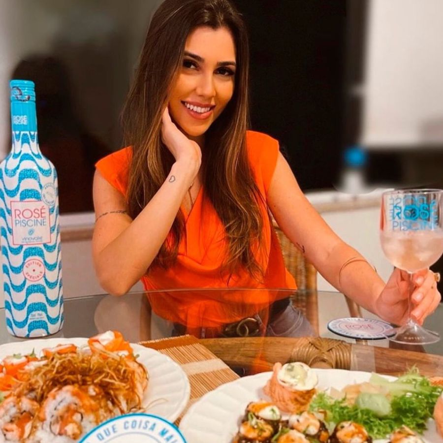 Mulher com taça de vinho rosé em frente a dois pratos com sushis de sabores variados