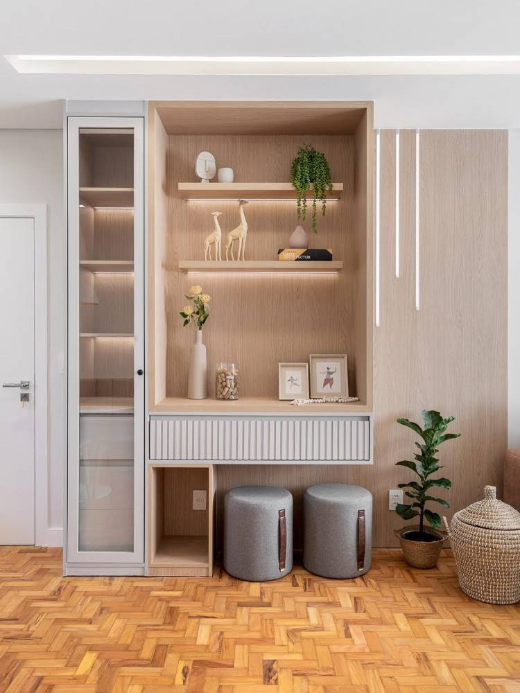 Apartamento clean com estante clean, em tons neutros. Uma parte é fechada com vidro e a outra abriga vaso de planta, pequenos quadros e outros itens decorativos. 