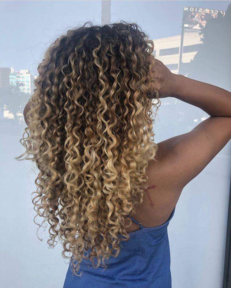 Mulher de pele morena com cabelo loiro cacheado solto