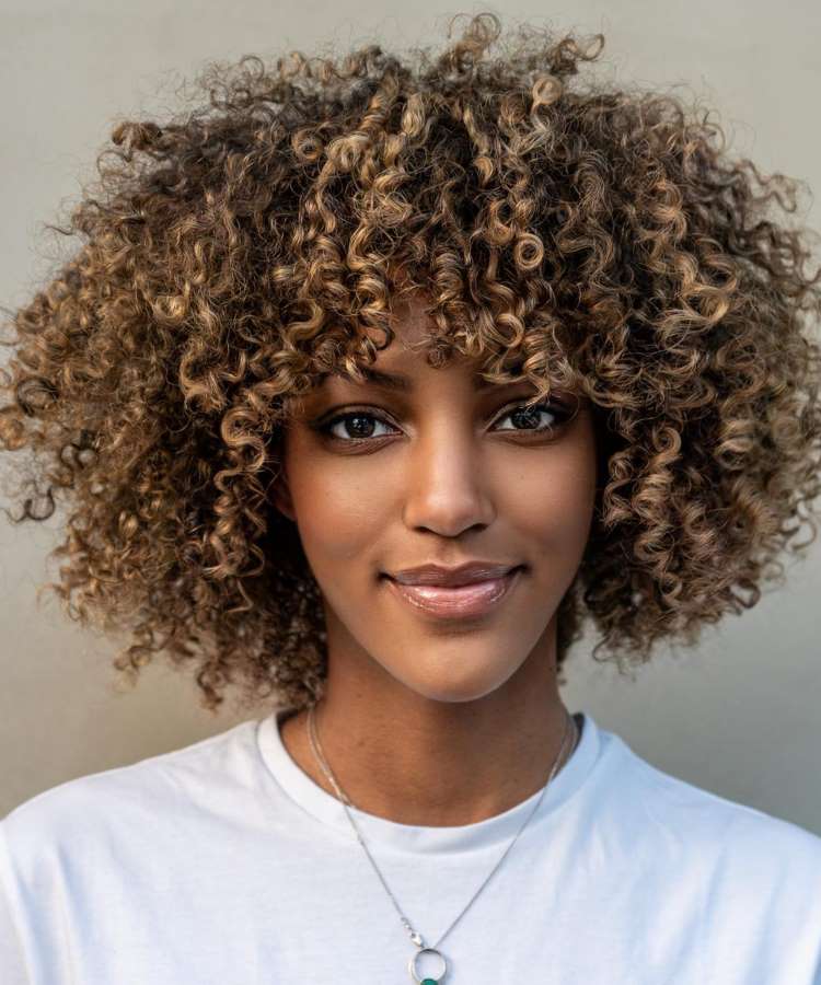 Mulher negra com cabelo crespo castanho iluminado e repicado