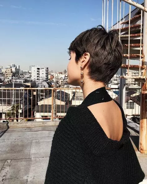 menina de costas com corte de cabelo curto, usando roupa de lã preta em prédio