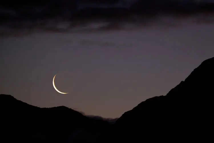 Foto de montanhas à noite. No céu, vemos a Lua Nova