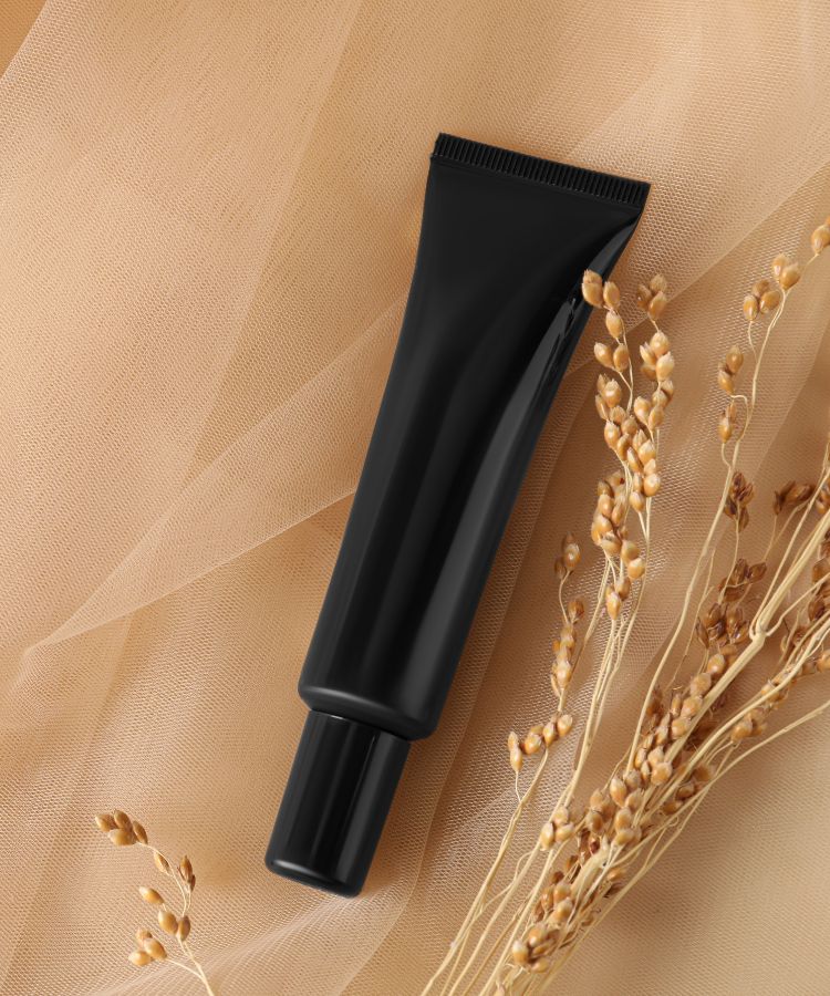 A imagem apresenta um tubo preto de base em creme sobre um tecido bege, com ramos secos ao lado. O fundo suave destaca o produto. Este é um dos tipos de base que oferece cobertura prática e uniforme, ideal para um acabamento natural e sofisticado na maquiagem.


