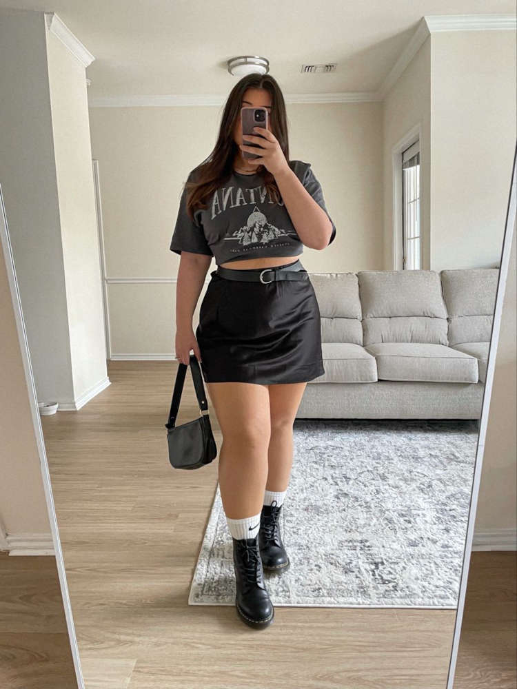 Mulher de pele clara com camiseta de banda cropped cinza e saia preta 
