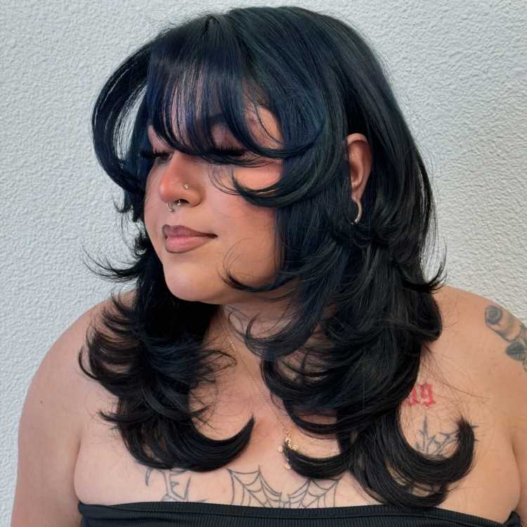 A imagem mostra uma pessoa com um corte de cabelo médio, repicado e em camadas. O cabelo tem volume e movimento, com as pontas viradas para fora, criando um visual dinâmico. A franja é longa e também repicada, emoldurando o rosto de forma suave. Esse estilo é frequentemente chamado de "corte em camadas repicadas" ou "corte shaggy", que é popular por adicionar textura e leveza ao visual.


