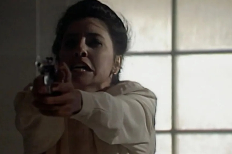 Cássia Kiss de branco com arma na mão