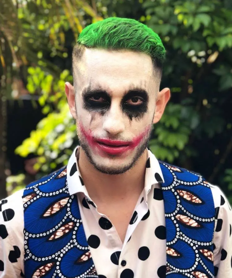 Homem maquiado de coringa para o Halloween, com cabelo verde, olhos pretos, boca vermelha 