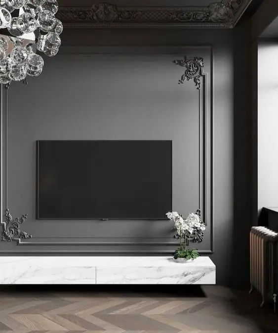 Sala de TV com parede escura com moldura trabalhada, aparador de mármore e vaso com flor branca 