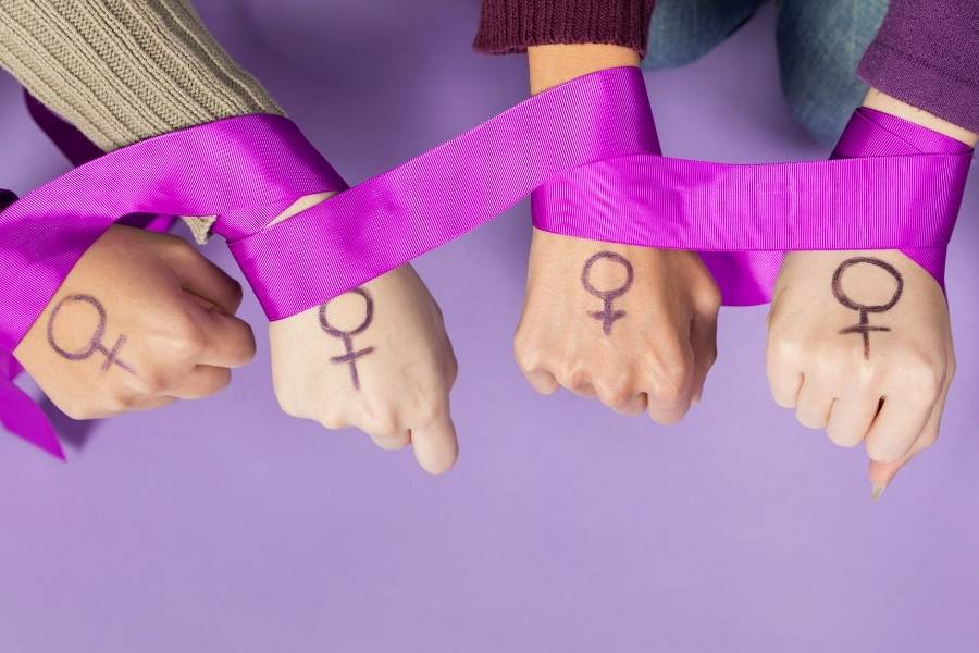 Mãos de mulheres enroladas com faixa lilás.