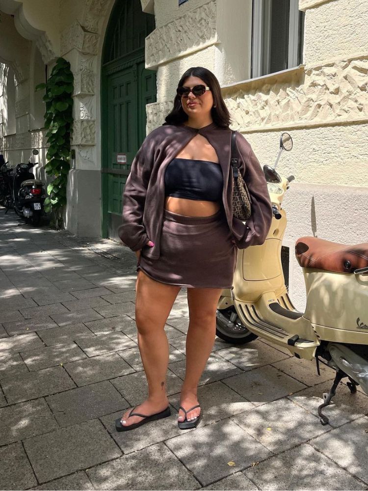mulher usando top faixa e chinelo pretos com saia e casaco marrons
