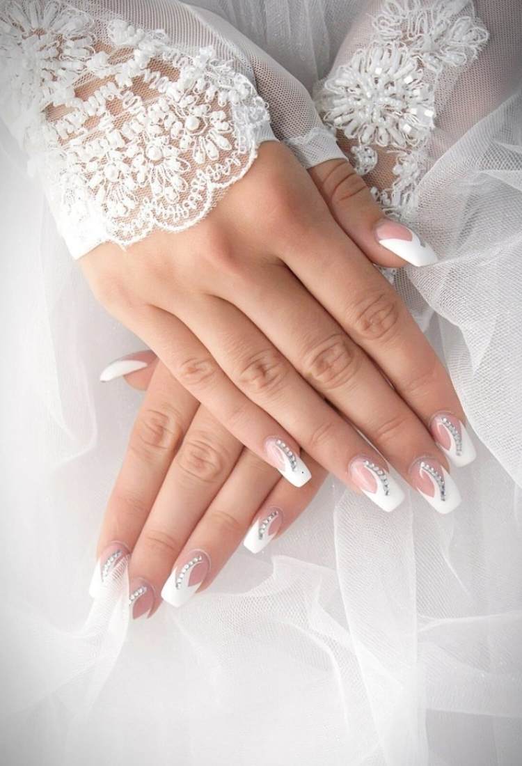 Unhas brancas quadradas com fundo transparente, detalhe branco nas pontas e meio, além de pedrarias 