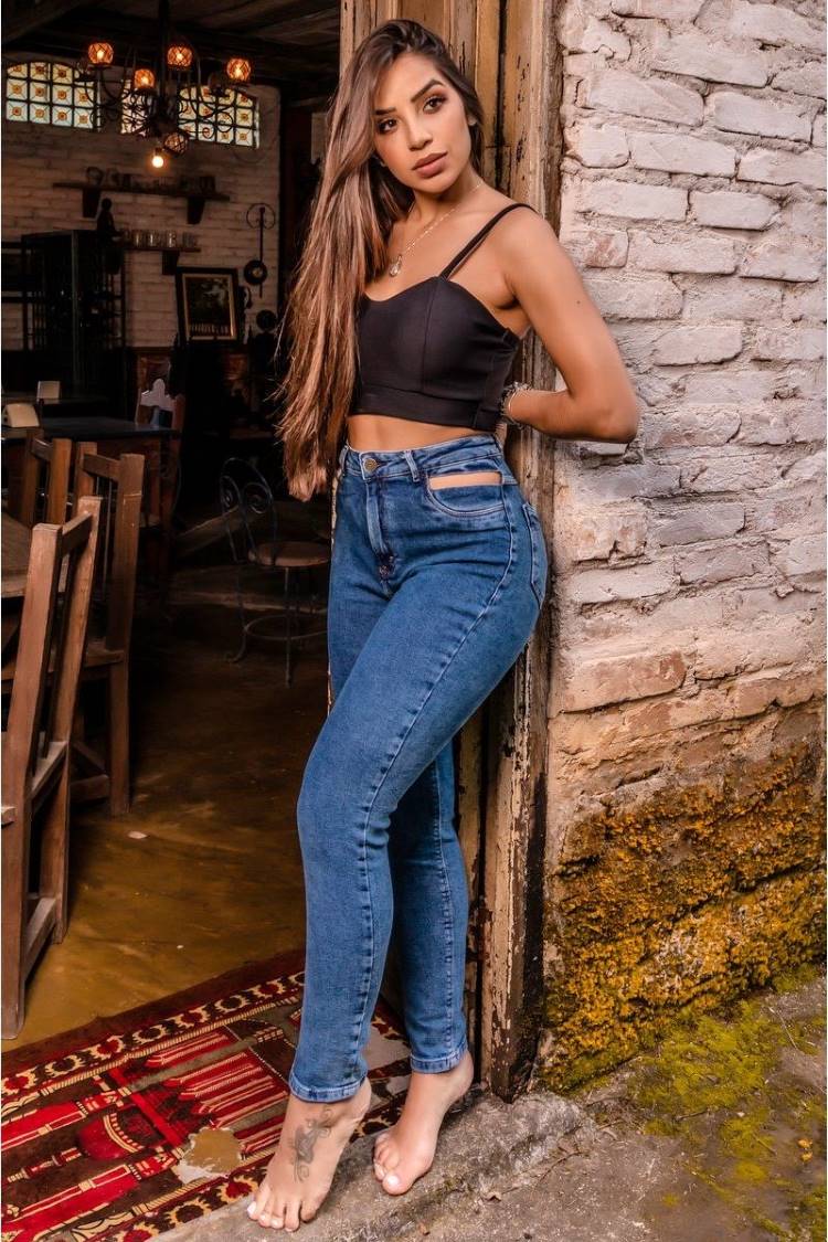 Mulher de pele clara de cropped preto e calça jeans com recorte na cintura