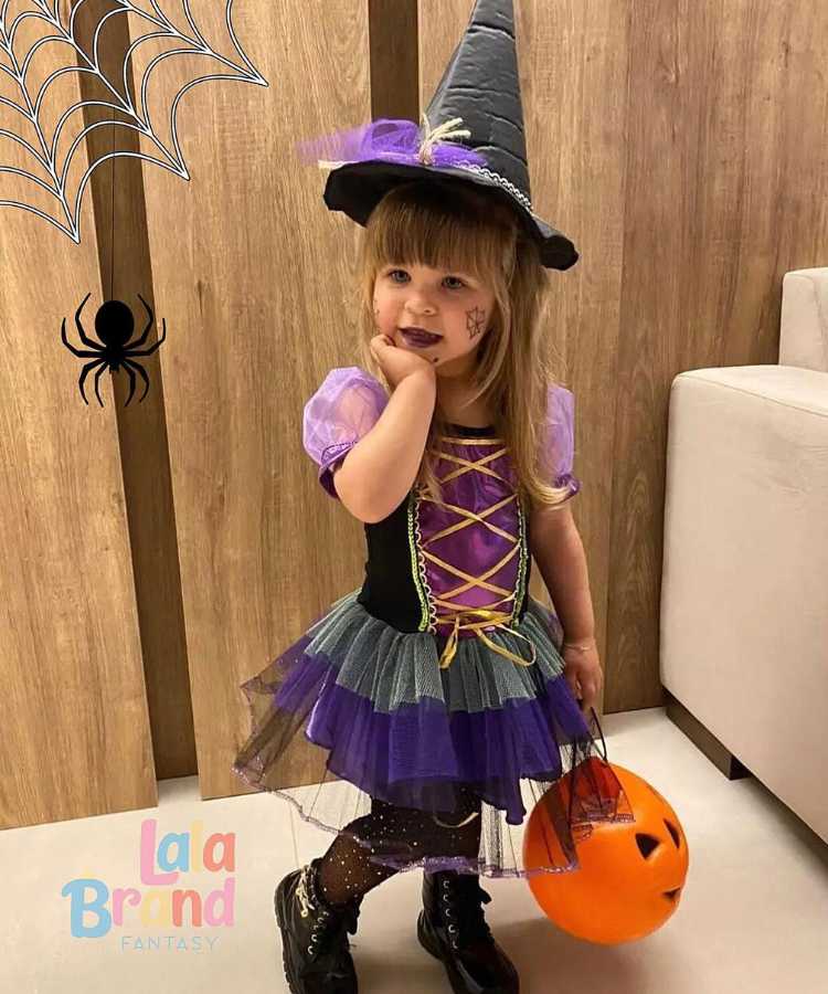 Garota fantasiada de bruxinha.Cores predominantes: preto, roxo, verde. Usa: vestido, meia calça com strass, botinha, chapéu pontudo, segura baldinho formato cabeça de abóbora