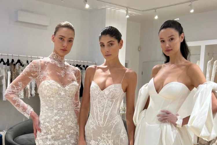 Três mulheres de pele clara usando vestidos de noiva de alcinhas e maquiagem minimalista, sendo duas com o cabelo preso e uma com o cabelo semi preso