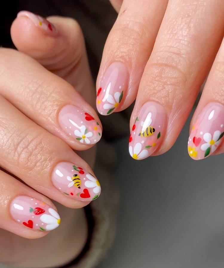 Unhas de gel decoradas com esmalte nude translúcido e desenhos delicados de flores brancas, corações vermelhos, abelhas e folhas verdes. O design criativo e alegre remete à primavera, combinando elementos vibrantes e delicadeza em um acabamento brilhante.